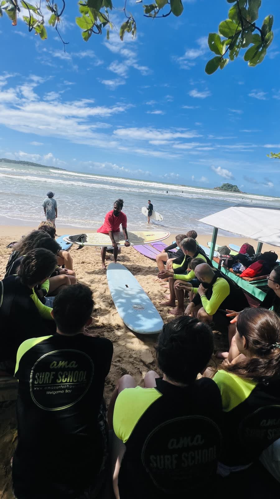 Surf lesson briefing on the beach in Weligama, with students sitting around an instructor and boards on the sand